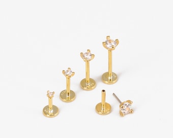 May include: Set of five gold-toned body jewelry pieces with clear crystal accents. The jewelry is in various sizes and styles, including labret studs and barbells.
