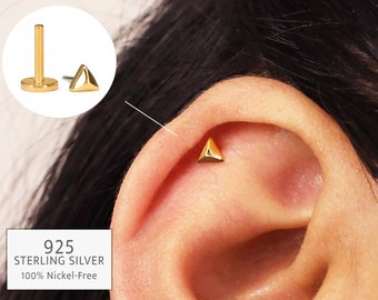May include: Gold triangle stud earring made of 925 sterling silver. The earring is nickel-free and is shown in a person's ear.