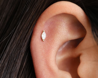 May include: A close-up of a person's ear with a small, gold, marquise-shaped diamond stud earring.