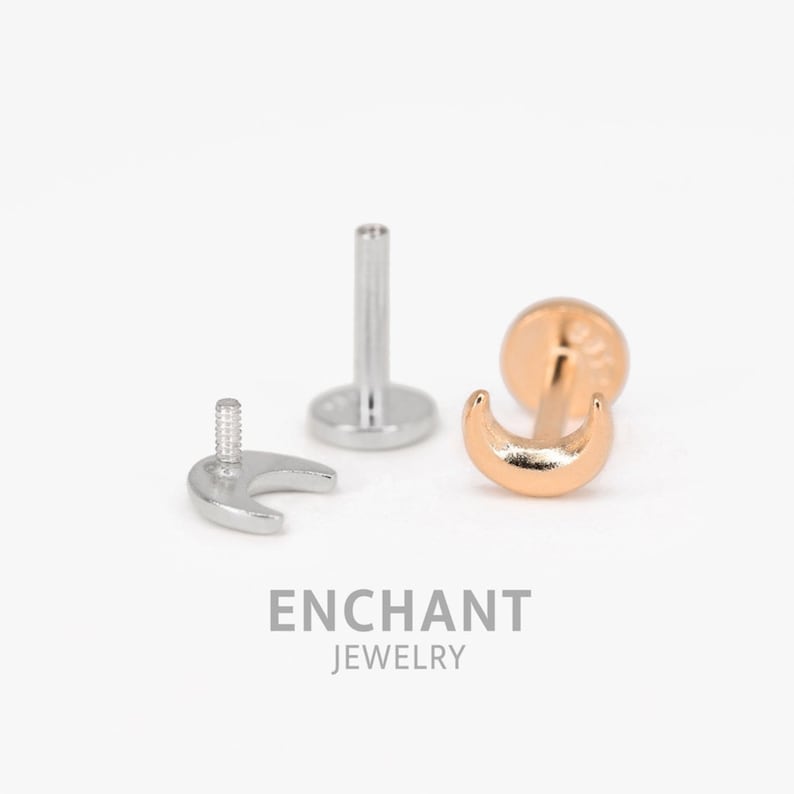 May include: A gold crescent moon shaped body jewelry piece with a silver post and back. The jewelry is shown disassembled with the post and back separate from the moon.