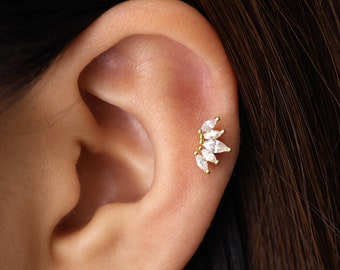 May include: A close-up of a person's ear with a gold ear cuff featuring a row of clear marquise-shaped stones.