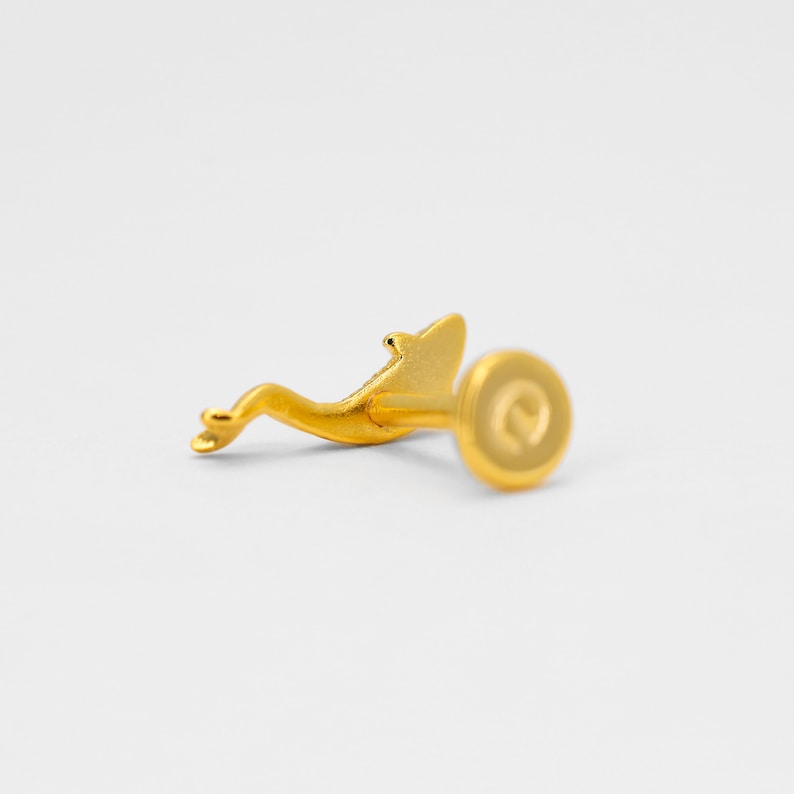 May include: Gold dolphin stud earring with a post and a round back. The back has a small letter "D" engraved on it.