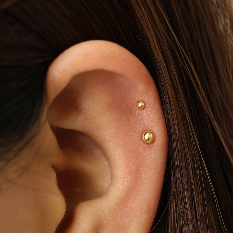 Puede incluir: Primer plano de una oreja con tres peque&ntilde;os pendientes de oro.