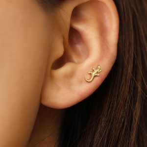 May include: Gold-toned lizard stud earring. The earring is small and delicate, and features a detailed lizard design.