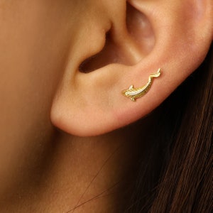 May include: Gold-toned dolphin stud earring. The dolphin is facing left and has a textured surface.