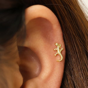 May include: Gold-toned lizard shaped stud earring. The earring is worn in the cartilage of the ear.