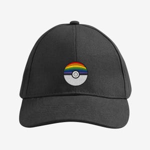 May include: A black baseball cap with a rainbow design. The design is a half-circle with a rainbow gradient and a white and grey bottom half. The cap has a curved peak and a button on top.