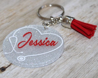 Può includere: Portachiavi a forma di cuore argentato con glitter, con un designo di stetoscopio bianco e il nome "Jessica" in lettere rosse. Il portachiavi ha un anello per chiavi argentato e un fiocco rosso.
