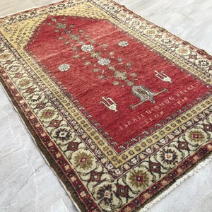 Puede incluir: Una alfombra de oración roja con un patrón floral y un borde beige. La alfombra tiene un borde con flecos y está hecha de lana.