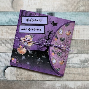 Pode incluir: Cartão roxo com o tema Halloween Wonderland. O cartão apresenta uma menina com cabelo loiro e uma abóbora, uma árvore assustadora e um relógio com corações e abóboras.