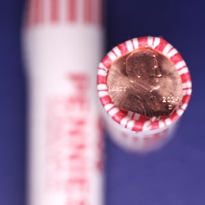 Op de afbeelding: Close-up van een rol pennies met een rood-wit gestreepte wikkel. Het uiteinde van de rol toont een penny met het jaartal 2025. Het woord "PENNIES" is zichtbaar op de zijkant van de rol.