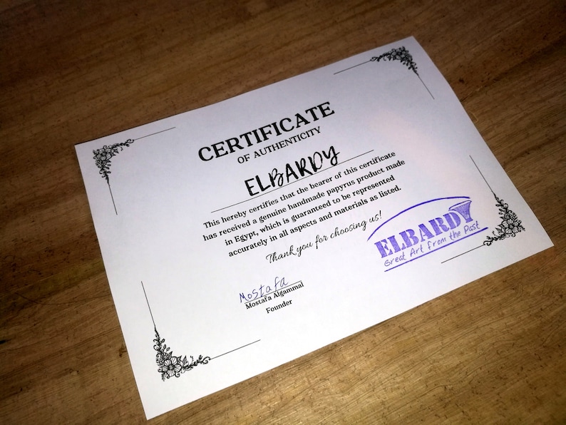 May include: A white certificate of authenticity with black text and a purple stamp. The certificate is for a handmade papyrus product from Elbardy, "Great Art from the Past".