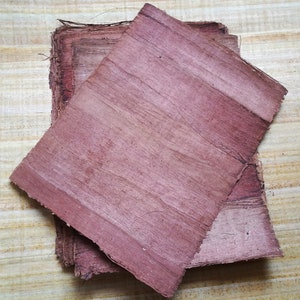 May include: Two sheets of reddish-brown papyrus paper, one on top of the other, with visible fibers. The paper is slightly wrinkled and has a textured surface.
