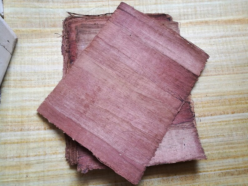 May include: Two sheets of reddish-brown papyrus paper, one on top of the other, with visible fibers. The paper is slightly wrinkled and has a textured surface.