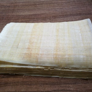 May include: A stack of papyrus sheets, a type of ancient paper made from the papyrus plant, with a light beige color and a slightly rough texture.