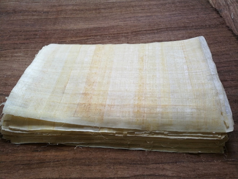 May include: A stack of papyrus sheets, a type of ancient paper made from the papyrus plant, with a light beige color and a slightly rough texture.