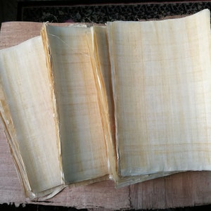 May include: A stack of several sheets of light beige papyrus paper. The paper has a woven texture and is slightly translucent.
