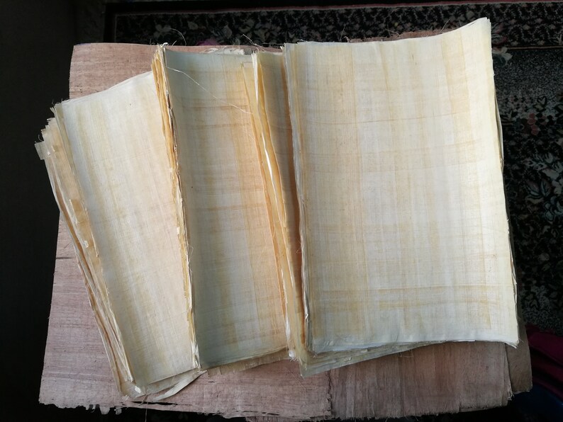 May include: A stack of several sheets of light beige papyrus paper. The paper has a woven texture and is slightly translucent.