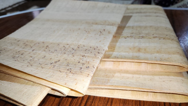May include: A stack of light brown papyrus sheets with visible fibers. The sheets are folded and have a slightly textured surface.