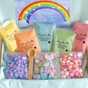 May include: A Rainbow Fizzy Potion Kit in an open box. The kit includes colorful powders in clear bags, a wooden spoon, and various candies. The box has a rainbow graphic and the text "Rainbow Fizzy Potion Kit".