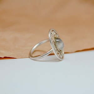 Op de afbeelding: Een zilveren ring met een delicaat, versierd ontwerp met een heldere edelsteen in het midden.