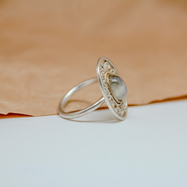 Op de afbeelding: Een zilveren ring met een delicaat, versierd ontwerp met een heldere edelsteen in het midden.