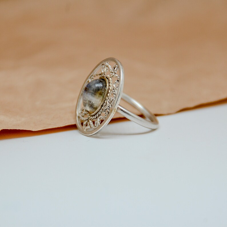 Op de afbeelding: Een zilveren ring met een grijze en witte steen in een filigraan ontwerp.