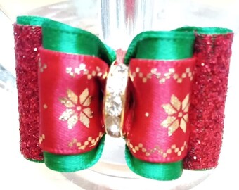 May include: A red and green Christmas bow with a gold snowflake pattern and a clear rhinestone in the center.