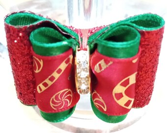 May include: A red and green Christmas-themed bow with gold candy cane and peppermint designs. The bow has a clear rhinestone in the center.