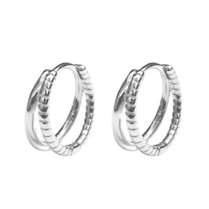 May include: A pair of silver hoop earrings. Each earring features a double-hoop design, with one smooth and one textured with a series of small, parallel lines. The earrings are displayed against a white background.