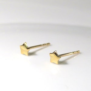 May include: A pair of small, gold-colored star-shaped stud earrings. The earrings have a simple, minimalist design with a post backing. The studs are set against a white background.