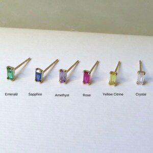 May include: Six pairs of stud earrings with rectangular gemstones in various colors: emerald, sapphire, amethyst, rose, yellow citrine, and crystal. Each earring has a gold-colored post.