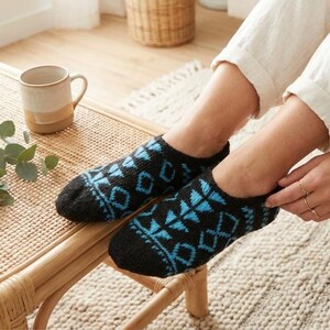 Puede incluir: Un par de calcetines tobilleros de punto negro con un patrón geométrico repetitivo en azul brillante. Los calcetines tienen un diseño de corte bajo que cubre el pie hasta el tobillo, mostrando una construcción de punto texturizado.