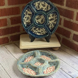 May include: Two ceramic serving platters. The top platter is blue with a dragonfly and fern pattern. The bottom platter is light blue with red and white designs. Both platters have multiple compartments.