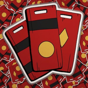 May include: A sticker featuring three rectangular red cards with rounded corners. Each card displays a white rectangular slot at the top, a horizontal black band, and a central yellow geometric shape, either a circle or a diamond, in a cartoon style.