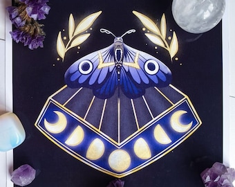 May include: A square print featuring a stylized moth with blue and purple wings, set against a dark background. The design includes a geometric shape with moon phases. Accompanying the print are purple flowers and crystals.