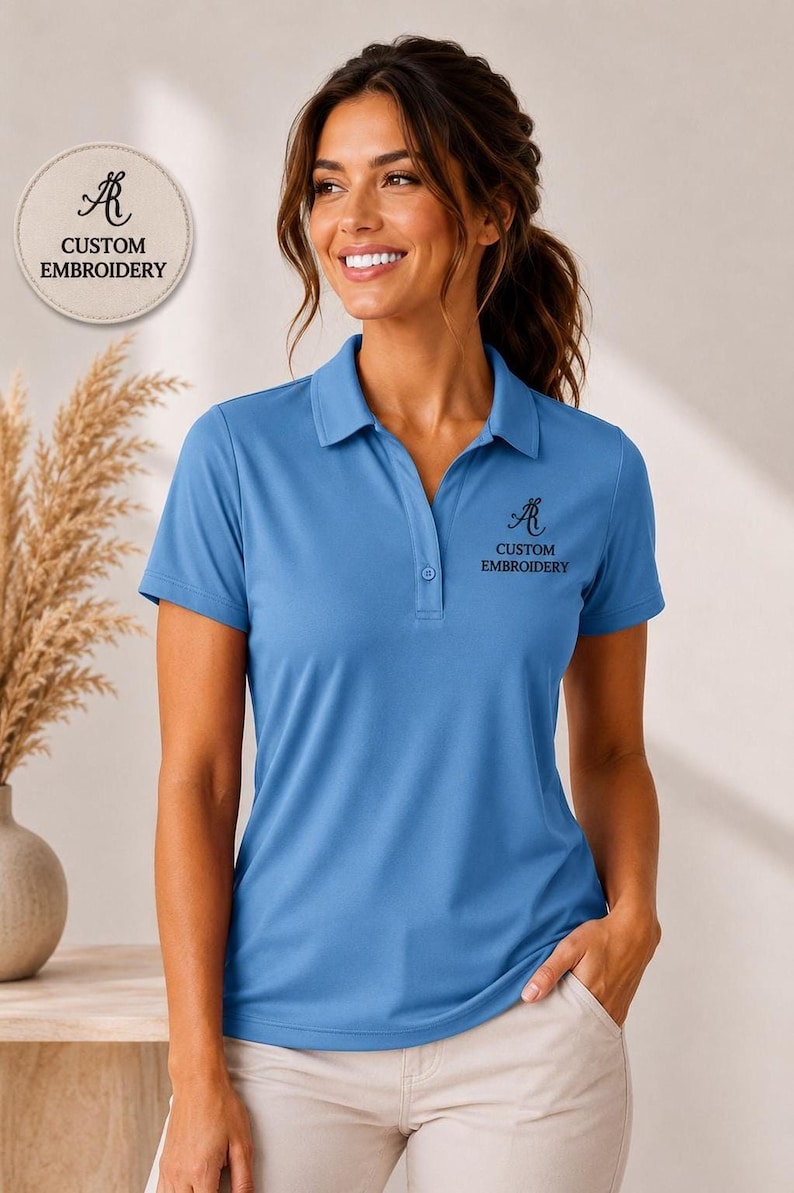 A woman wearing a blue polo shirt with the text "CUSTOM EMBROIDERY" on it, smiling and posing for the camera.
