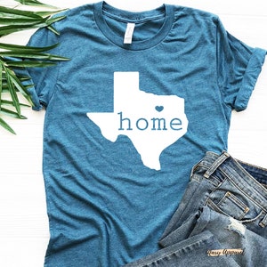 May include: A teal blue t-shirt with a white outline of the state of Texas and the word "home" inside. A small white heart is in the center of the state.
