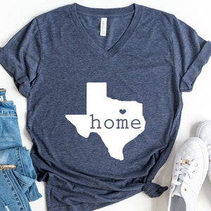 May include: A navy blue t-shirt with a white outline of the state of Texas and the word "home" inside. A small white heart is in the center of the state.