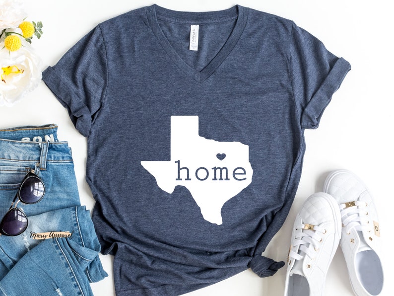 May include: A navy blue t-shirt with a white outline of the state of Texas and the word "home" inside. A small white heart is in the center of the state.