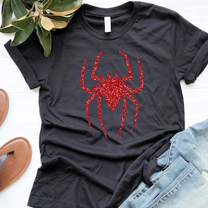 K&ouml;nnte beinhalten: Schwarzes T-Shirt mit einem roten Glitzer-Spinnen-Motiv.