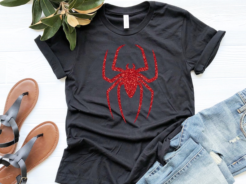 K&ouml;nnte beinhalten: Schwarzes T-Shirt mit einem roten Glitzer-Spinnen-Motiv.