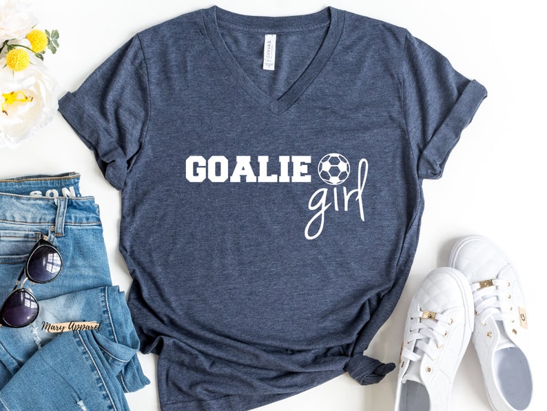 Op de afbeelding: Een marineblauw V-hals T-shirt met de tekst "GOALIE girl" in wit, met een witte voetbalafbeelding.