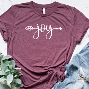 May include: A maroon t-shirt with a white graphic of an arrow with a leaf and the word "joy" written in cursive.