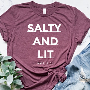 May include: A maroon t-shirt with the text "SALTY AND LIT" in white lettering. The text "Matt 5:13" is printed below the main text.