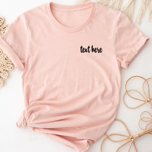 May include: A light pink t-shirt with the text "text here" in black lettering on the front.