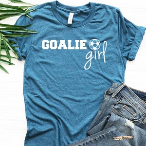 Op de afbeelding: Tealblauw T-shirt met witte tekst "Goalie girl" en een witte voetbalafbeelding.