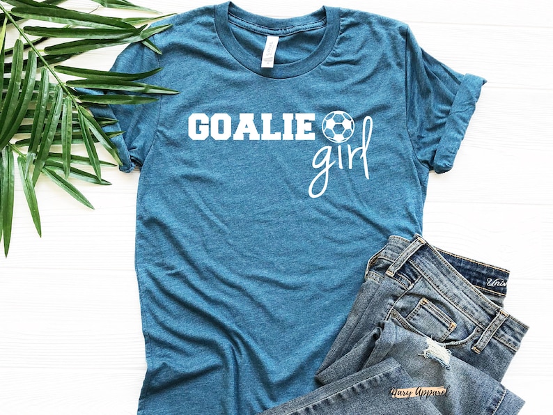 Op de afbeelding: Tealblauw T-shirt met witte tekst "Goalie girl" en een witte voetbalafbeelding.