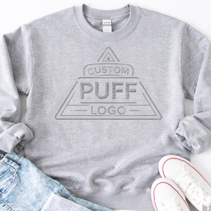 A gray sweatshirt with a logo printed on it, along with a pair of jeans and white sneakers.