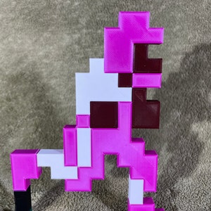 May include: A pink and white pixelated flamingo figurine. The flamingo is standing on one leg with its head tilted to the side. The figurine is made of plastic and has a 3D printed look.